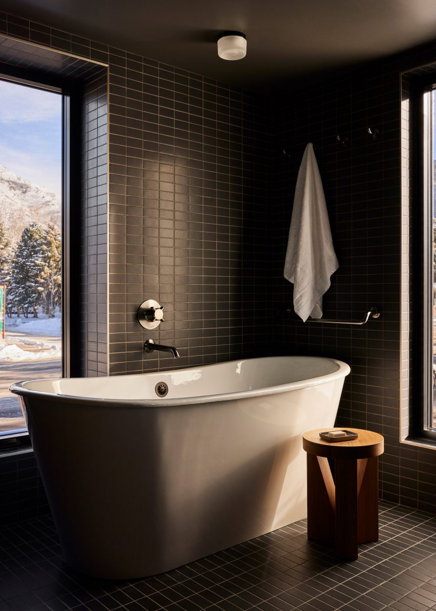 Cuarto de baño con azulejos de color verde oscuro y bañera blanca.