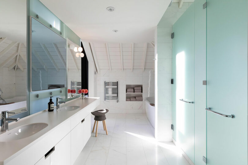 Cuarto de baño moderno con lavabo doble, espejo grande, paredes de azulejos blancos y puertas de cristal esmerilado.