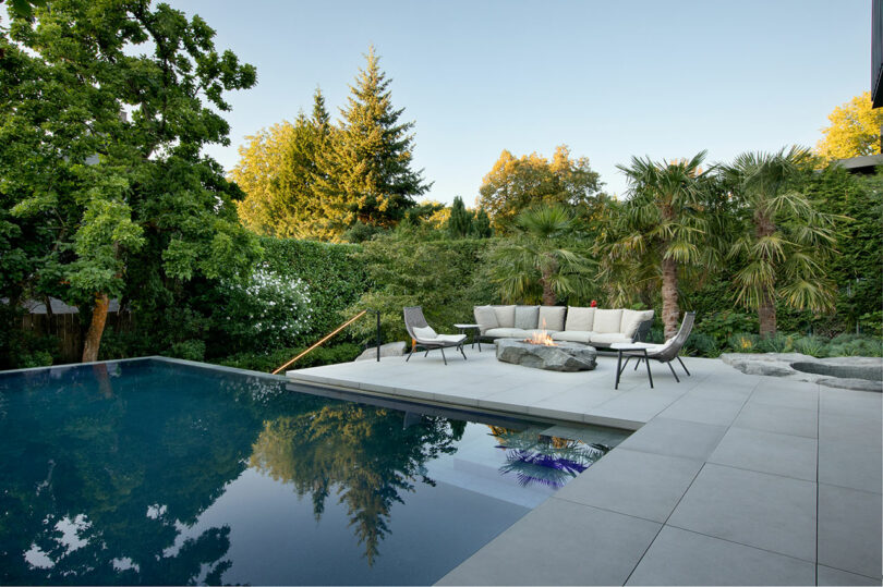 Un lujoso patio con piscina, modernos muebles de jardín y exuberante vegetación bajo un cielo despejado.