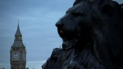BBC Primer plano de la cabeza de un león en Trafalgar Square con la Torre Isabel de las Casas del Parlamento al fondo