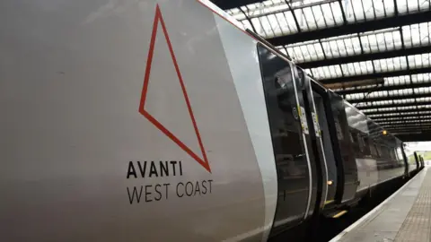 Getty Images Toma lateral de un tren parado en una estación de tren. En el lateral está el contorno de un triángulo naranja que es el logotipo de Avanti West Coast. Y también es legible. 