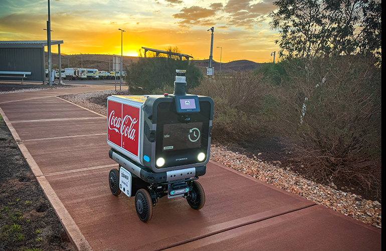 Imagen heroica del robot de reparto ottobot al atardecer, conduciendo por una acera.
